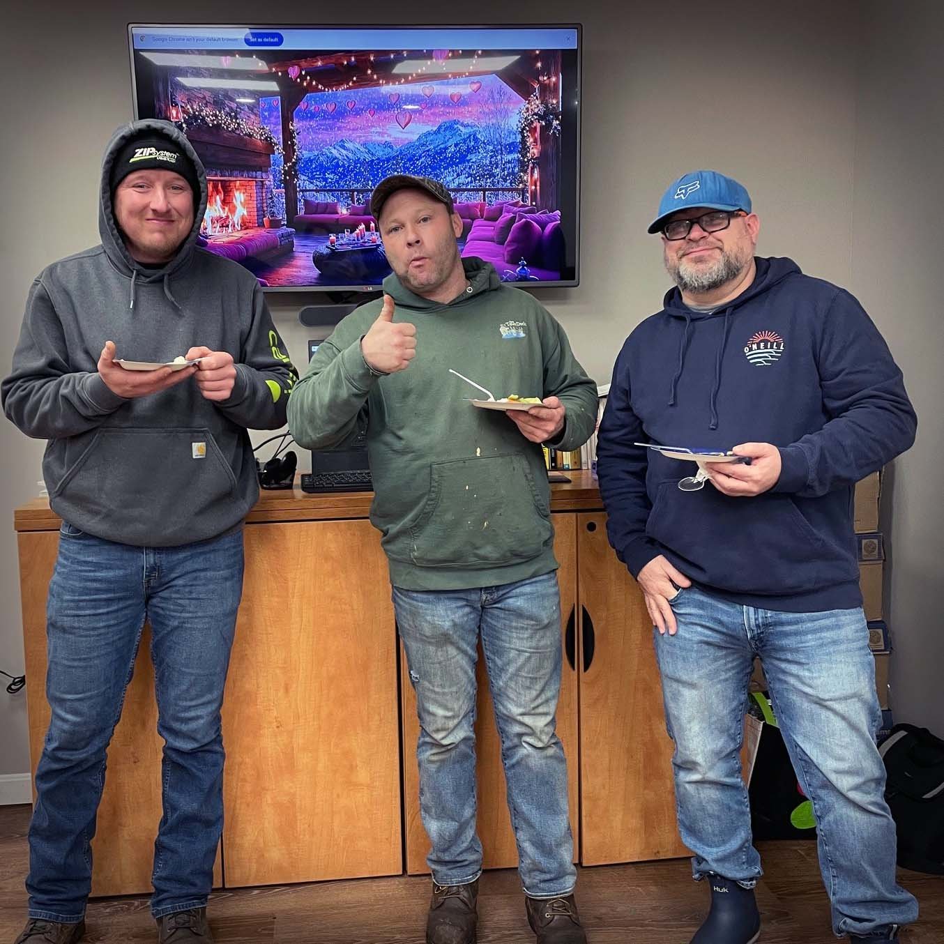 Three employees in hoodies and jeans enjoying their snacks. One gives a thumbs up.