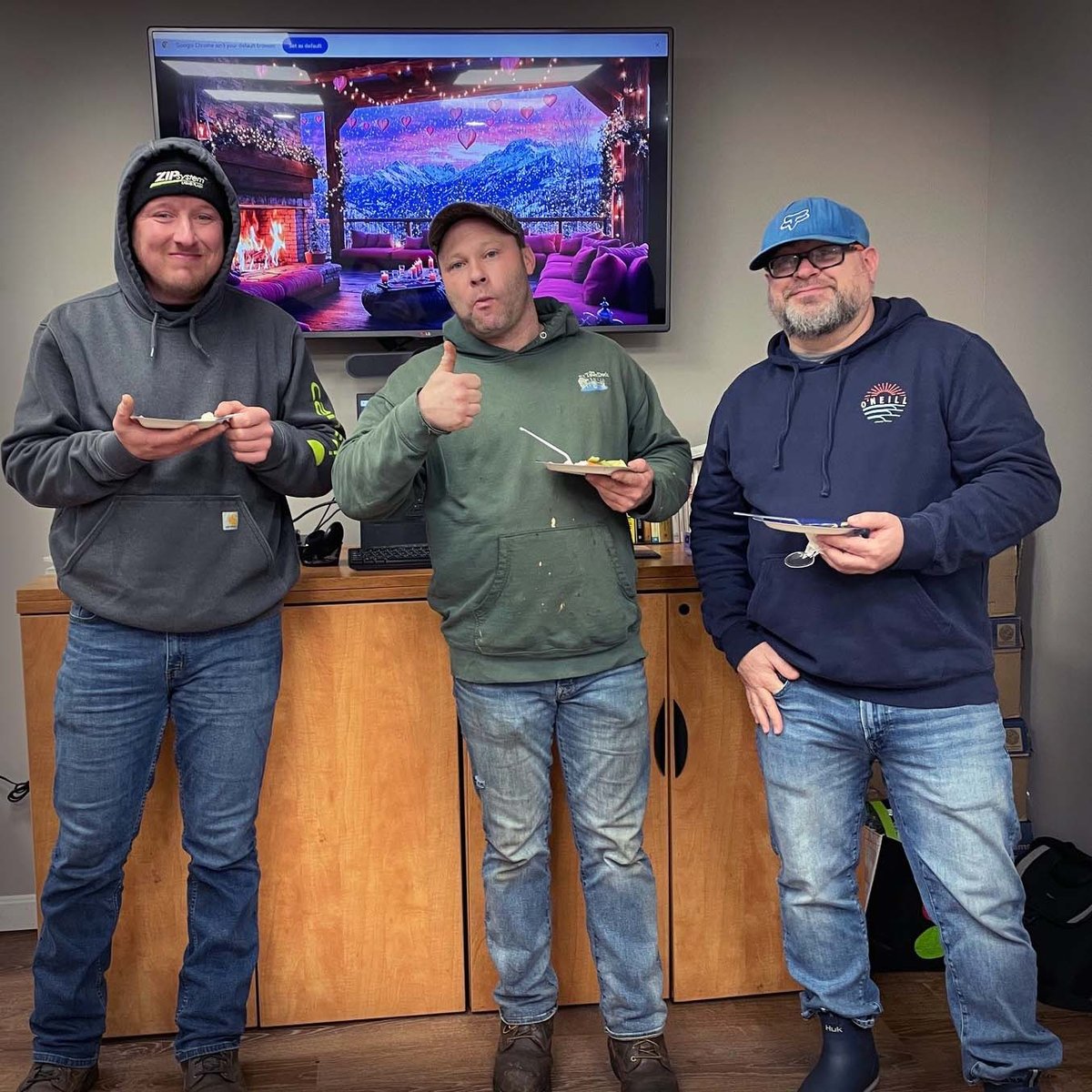 Three employees in hoodies and jeans enjoying their snacks. One gives a thumbs up.