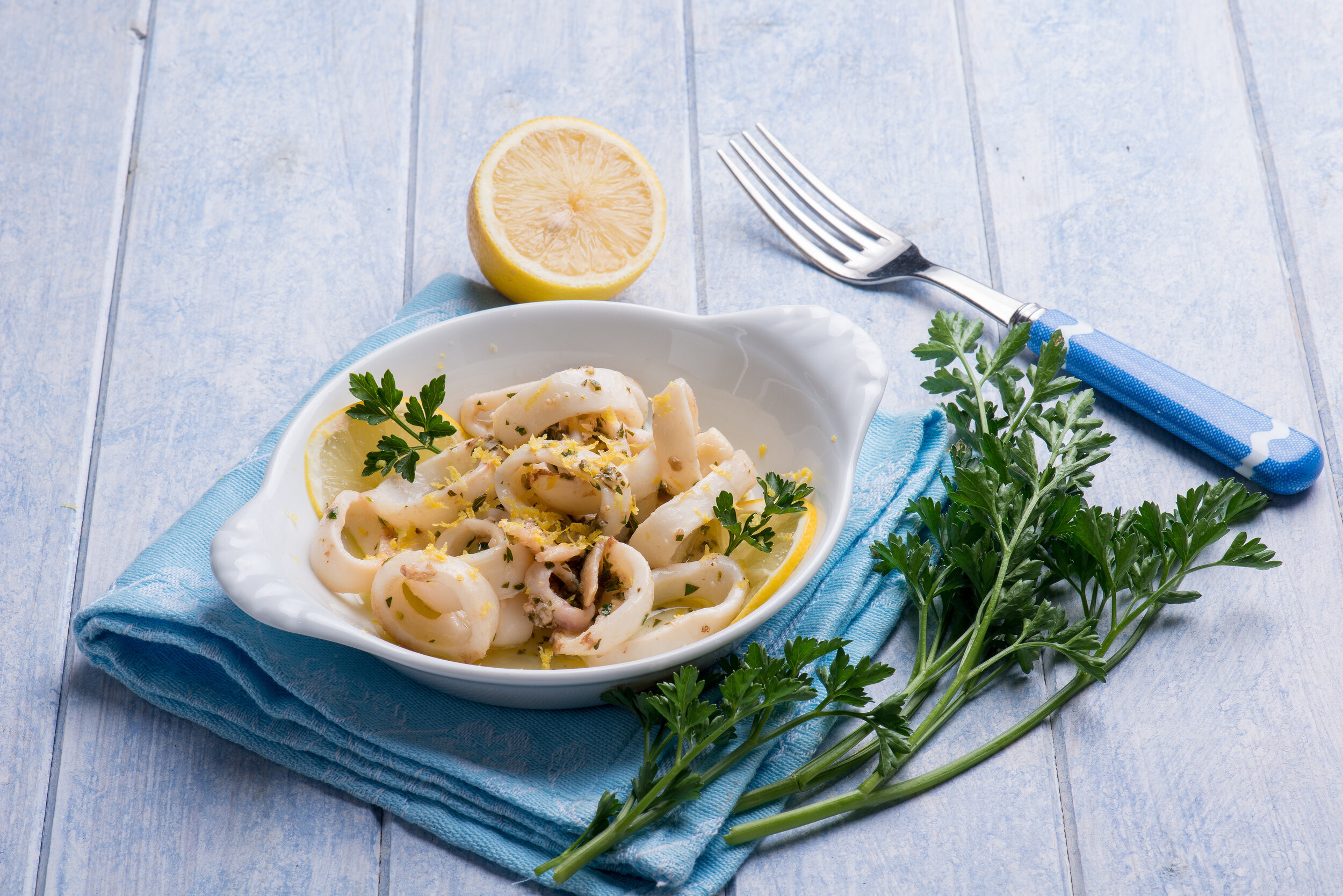 Certified sustainable calamari rings in a white dish, garnished with lemon and parsley.