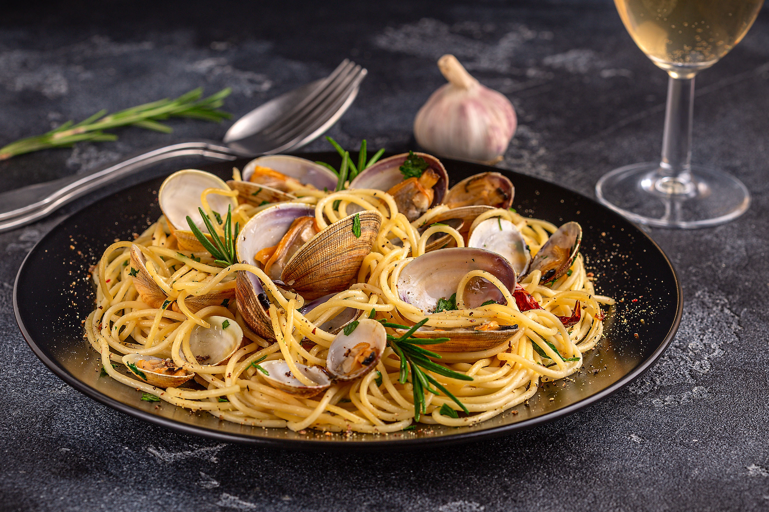 A black pasta bowl with spaghetti, whole shell clams, garlic and parsley